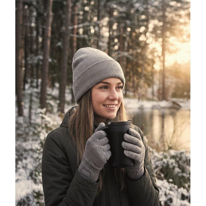 En kvinna håller en mörk mugg under en vinterpromenad i en solbelyst skog