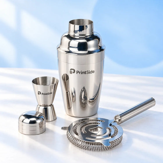Polished steel cocktail shaker, jigger and strainer with PrintSide branding.