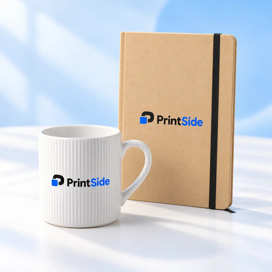 Anteckningsbok i kraftpapper och vit räfflad keramikmugg med PrintSide-logotyper.