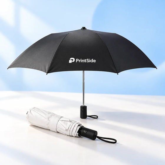 Open black umbrella with a PrintSide logo beside a folded white umbrella.